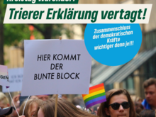 Demonstrierende Menschen, freundlich aussehend, mit Regenbogenfahnen und Plakaten