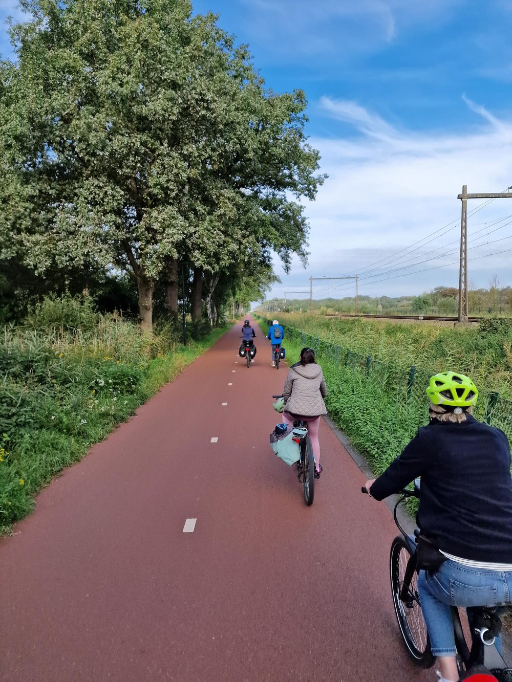Mitglieder der Kreistagsfraktion fahren in Holland mit ihren Rädern auf einem Radschnellweg entlang einer Bahntrasse, rechts und links breite Grünstreifen, blauer Himmel