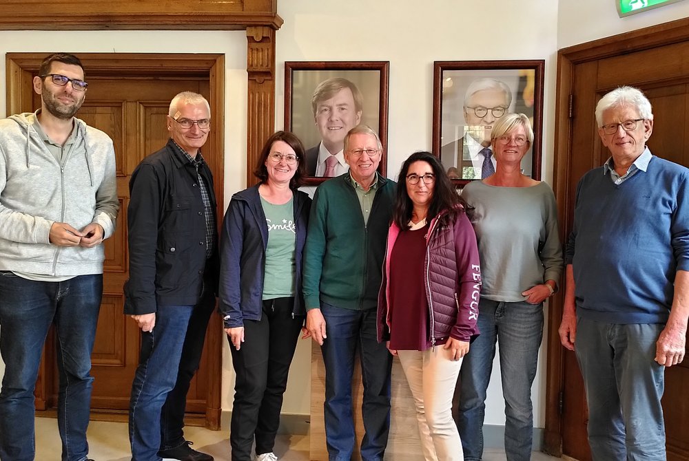 Gruppenbild, Stehende Menschen vor einem Bild von dem niederländischen König Willem Alexander und dem deutschen Bundespräsidenten Frank-Walter Steinmeiersch über On-Demand-Verkehr, Gruppenbild in der EUREGIO-Zentrale am deutsch-niederländischen Grenzübergang Gronau-Enschede